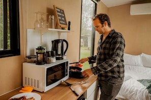 Une personne cuisine dans une petite cuisine équipée d’un four à micro-ondes, d’une machine à café et de divers ustensiles de cuisine.
