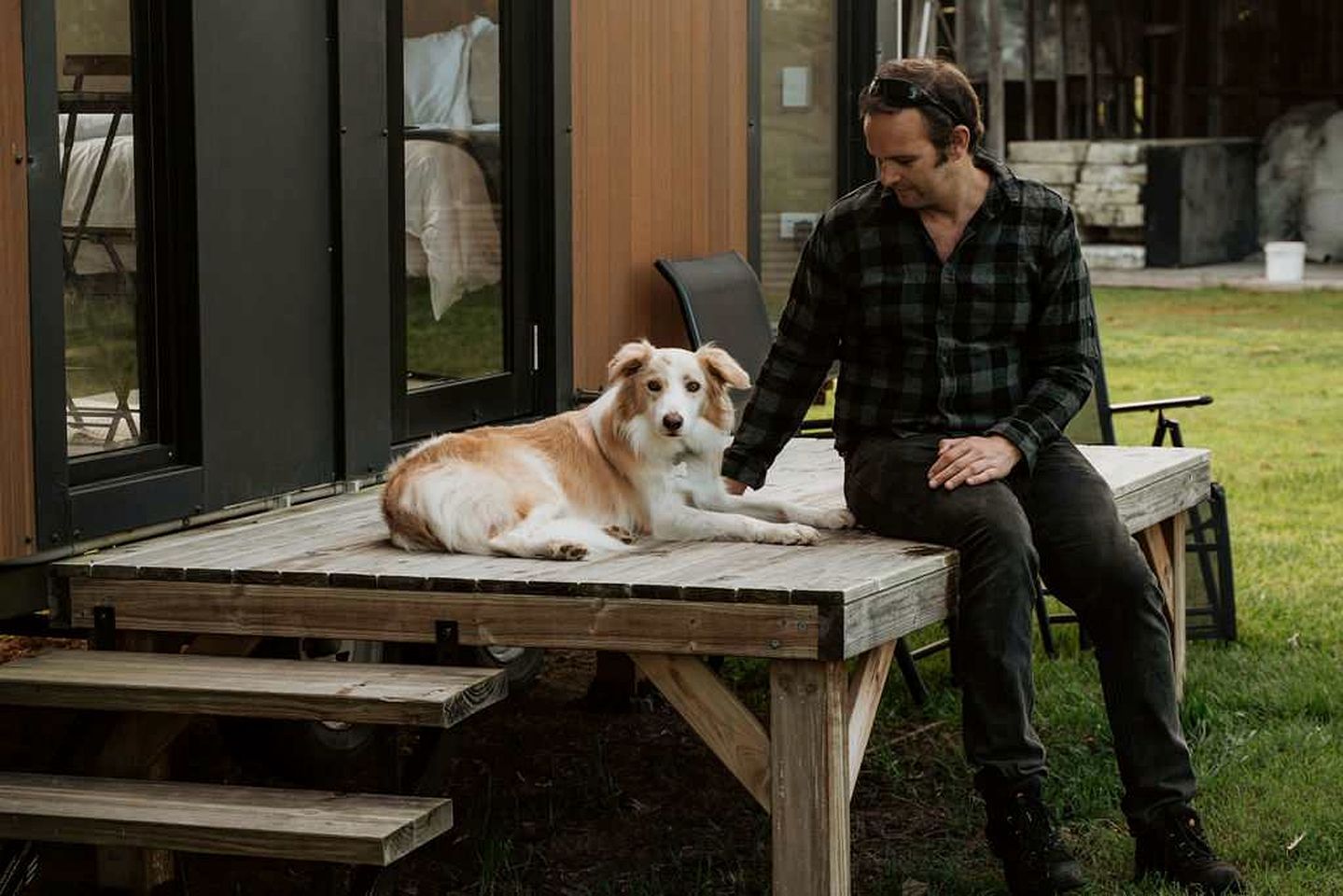 A person sitting on a wooden bench outdoors with a dog beside them.