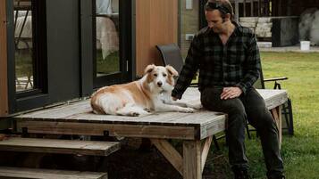 A person sitting on a wooden bench outdoors with a dog beside them.