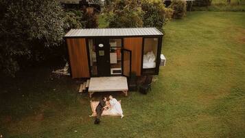 A small, single-story wooden structure with a porch, a bench, and a bed visible through the open door.