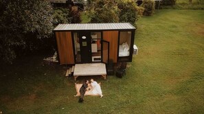 A small, single-story wooden structure with a porch, a bench, and a bed visible through the open door.