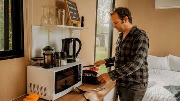 Une personne cuisine dans une petite cuisine équipée d’un four à micro-ondes, d’une machine à café et de divers ustensiles de cuisine.