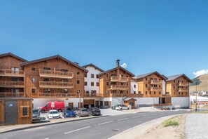 Ein mehrstöckiges Holzgebäude mit Balkonen, ein Parkplatz mit mehreren Autos und einem wolkenlosen Himmel.