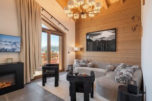 Ein modernes Wohnzimmer mit Kamin, einem großen Fenster mit Bergblick, einer gemütlichen Couch und einer zeitgemäßen Chandelieber.