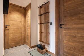 Ein Flur mit Holztüren, einem an der Wand befestigten Gestell und einem Korbwägelchen auf dem Boden.