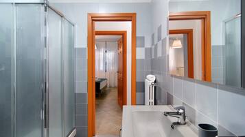 A modern bathroom with a glass shower enclosure, a sink with a mirror, and a hallway leading to a bedroom.