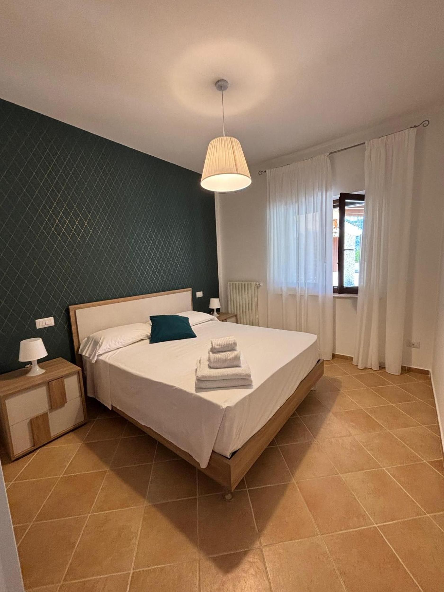 Een slaapkamer met een bed, nachtkastje, lamp en een raam met gordijnen.