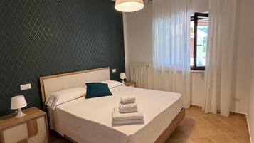 Een slaapkamer met een bed, nachtkastje, lamp en een raam met gordijnen.