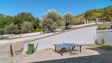 Un patio con mesa de ping pong, un bote de basura verde y una zona pavimentada.