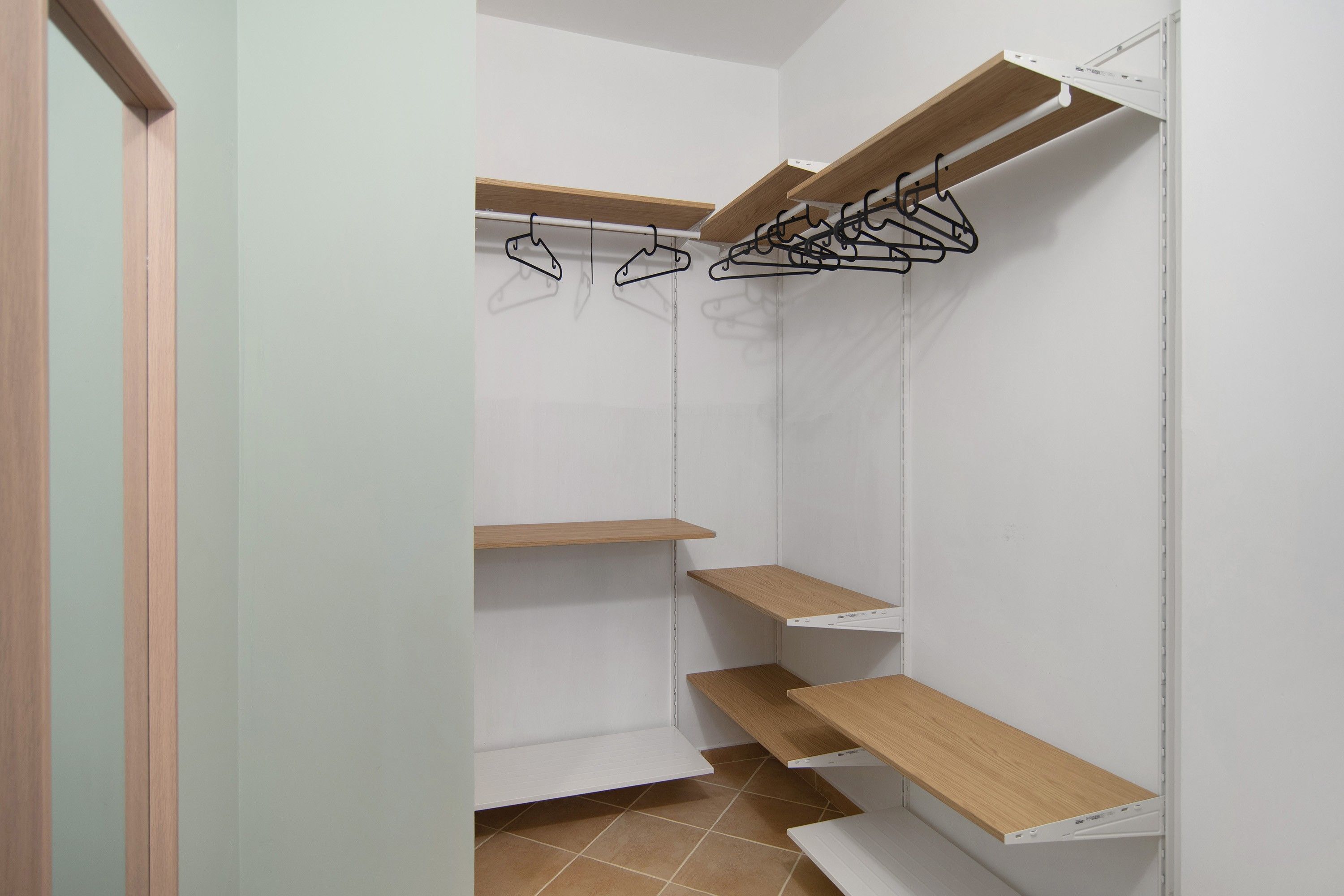 Ein begehbarer Kleiderschrank mit offenen Regalen, Holzboden und einer weißen Tür.