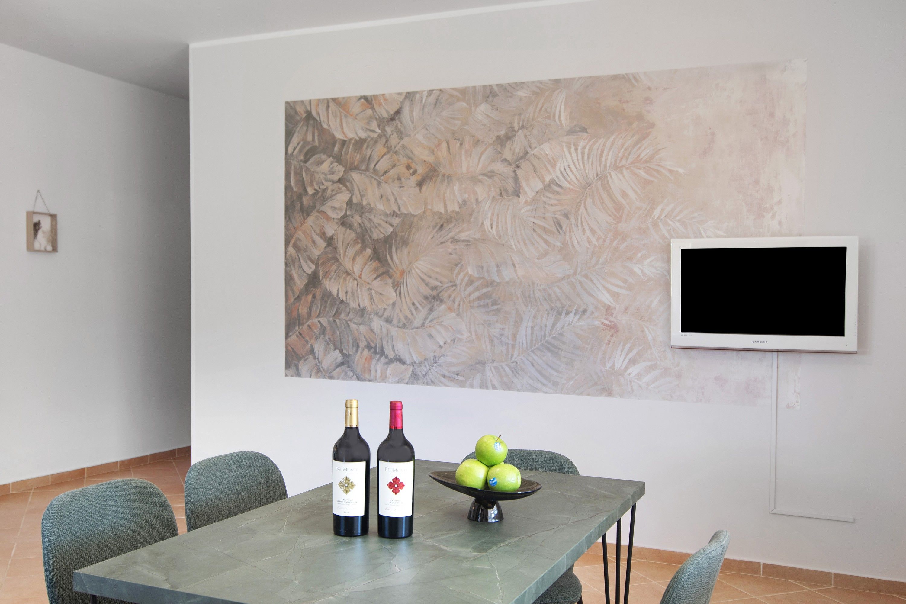 A dining area with a table, two wine bottles, and a bowl of apples.
