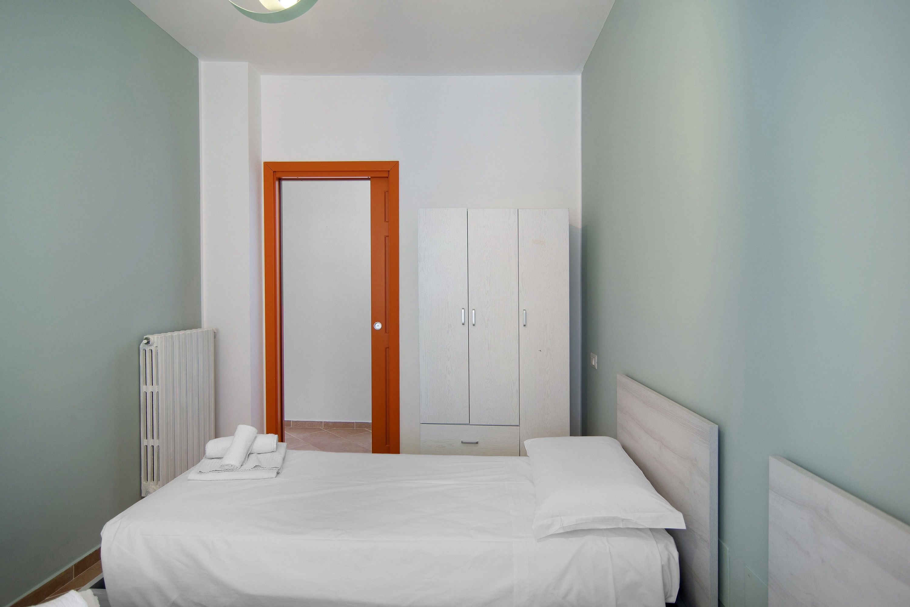 A bedroom with a bed, a radiator, a wardrobe, and a door leading to another room.