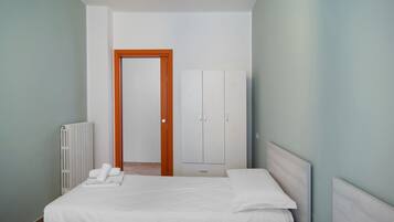 A bedroom with a bed, a radiator, a wardrobe, and a door leading to another room.