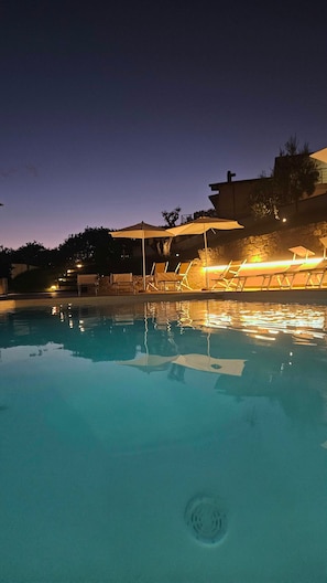 Una piscina amb gandules i ombrel·les, envoltada de murs de pedra i arbres.