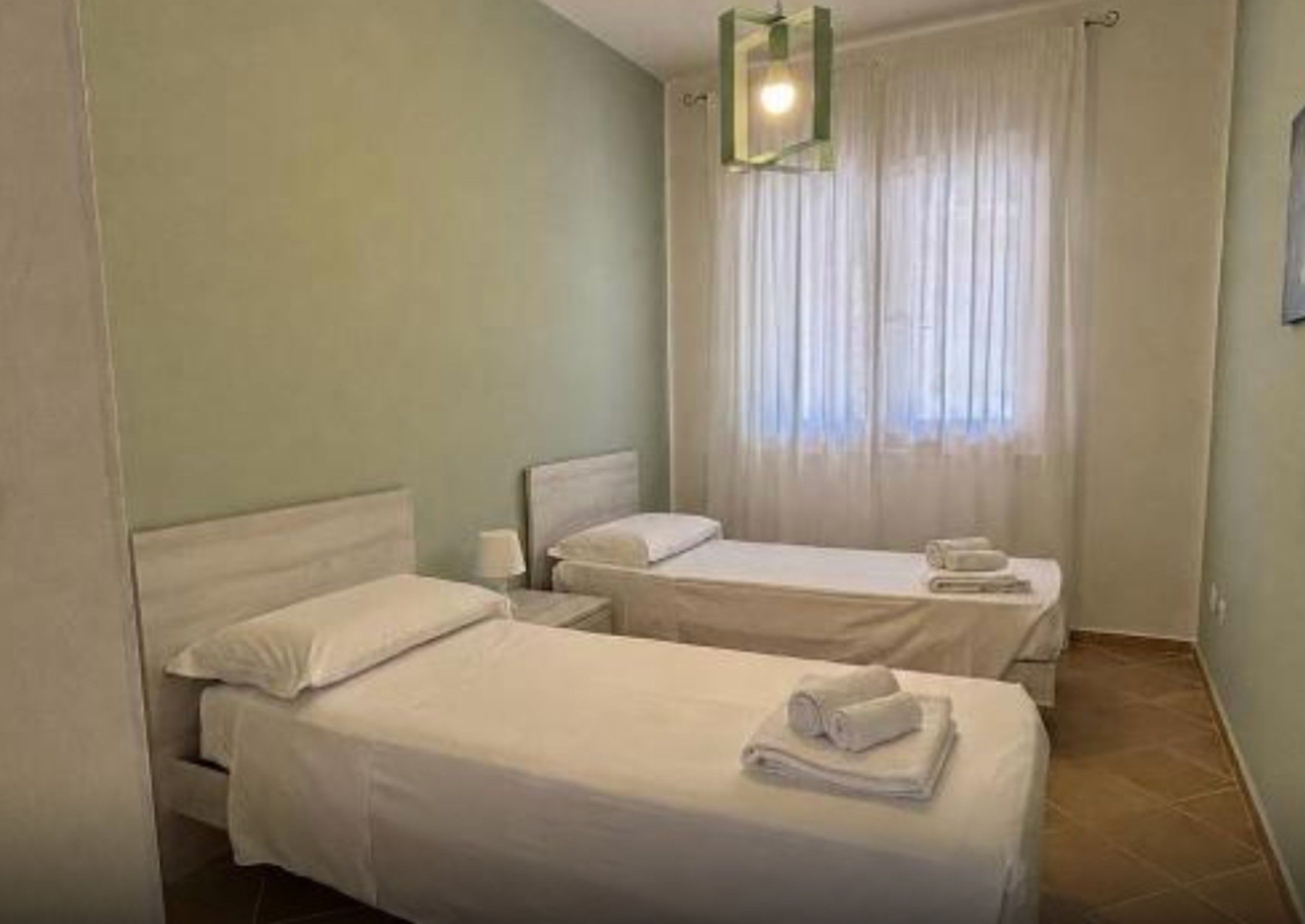 Una camera d'albergo con due letti singoli, un comodino, una lampada e una finestra con tende.