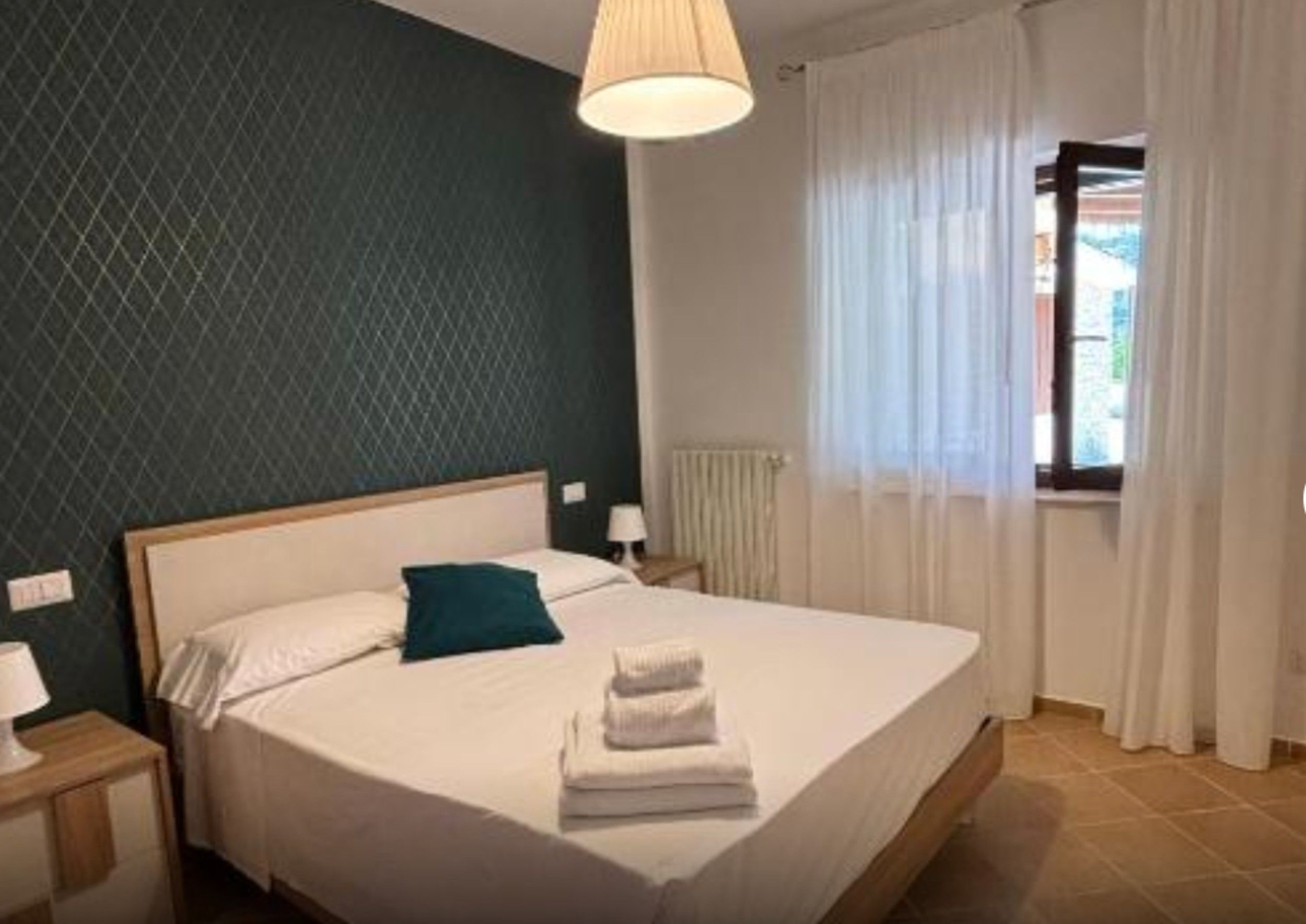 Una camera d'albergo con un letto, un comodino, una lampada e una finestra con tende.