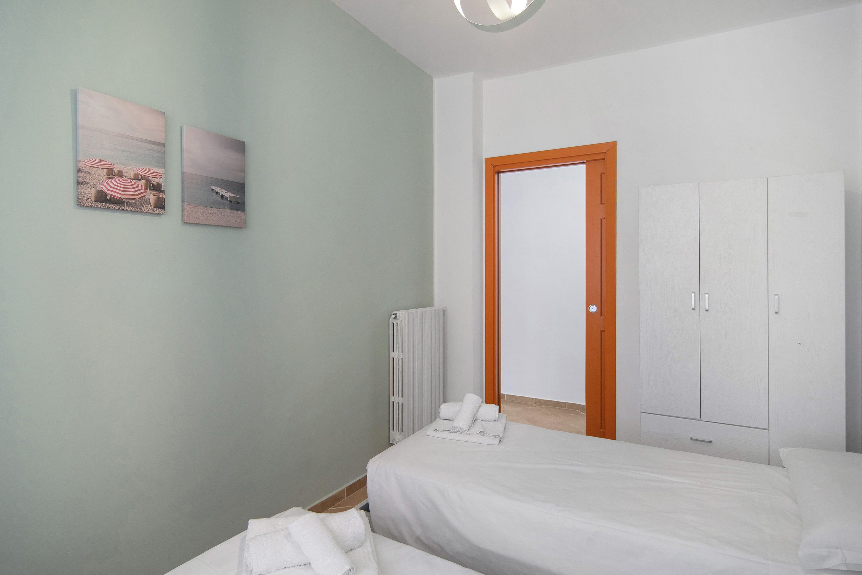 Ein Schlafzimmer mit zwei Betten, einem Heizkörper, einem Kleiderschrank und zwei gerahmten Bildern an der Wand.