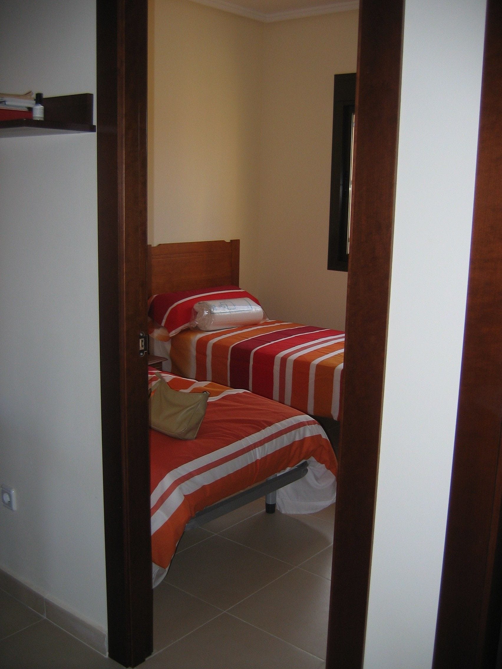 Een kleine hotelkamer met twee bedden, elk voorzien van gestreept beddengoed, een houten hoofdbord en een beige wand.