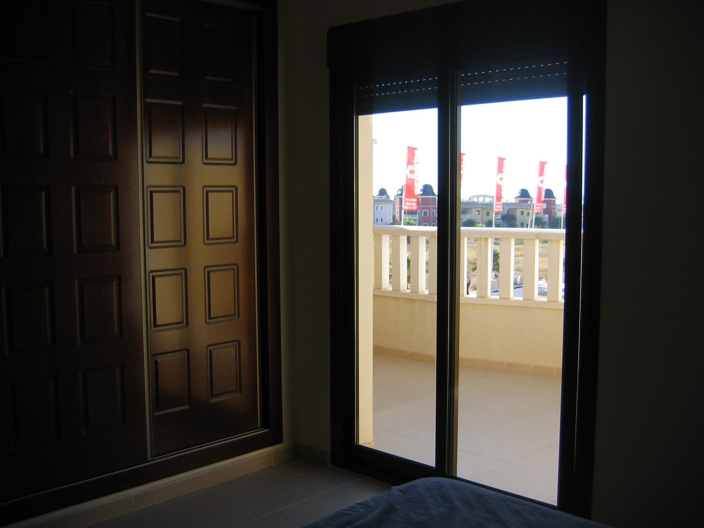 Een kamer met een groot raam, een donkere houten deur en uitzicht op gebouwen en een balkon.