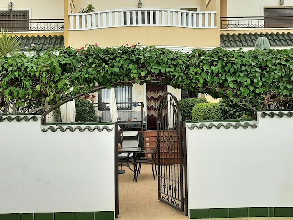 A gated entrance with a decorative archway, a tiled floor, and a view of a balcony and window.
