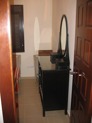 Een kleine kamer met een zwarte dressoir, een spiegel, een rieten mand en een radiator.