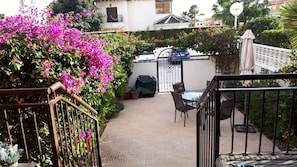 Een terras met een glazen tafel en stoelen, omringd door een tuin met roze bloemen en een witte hek.