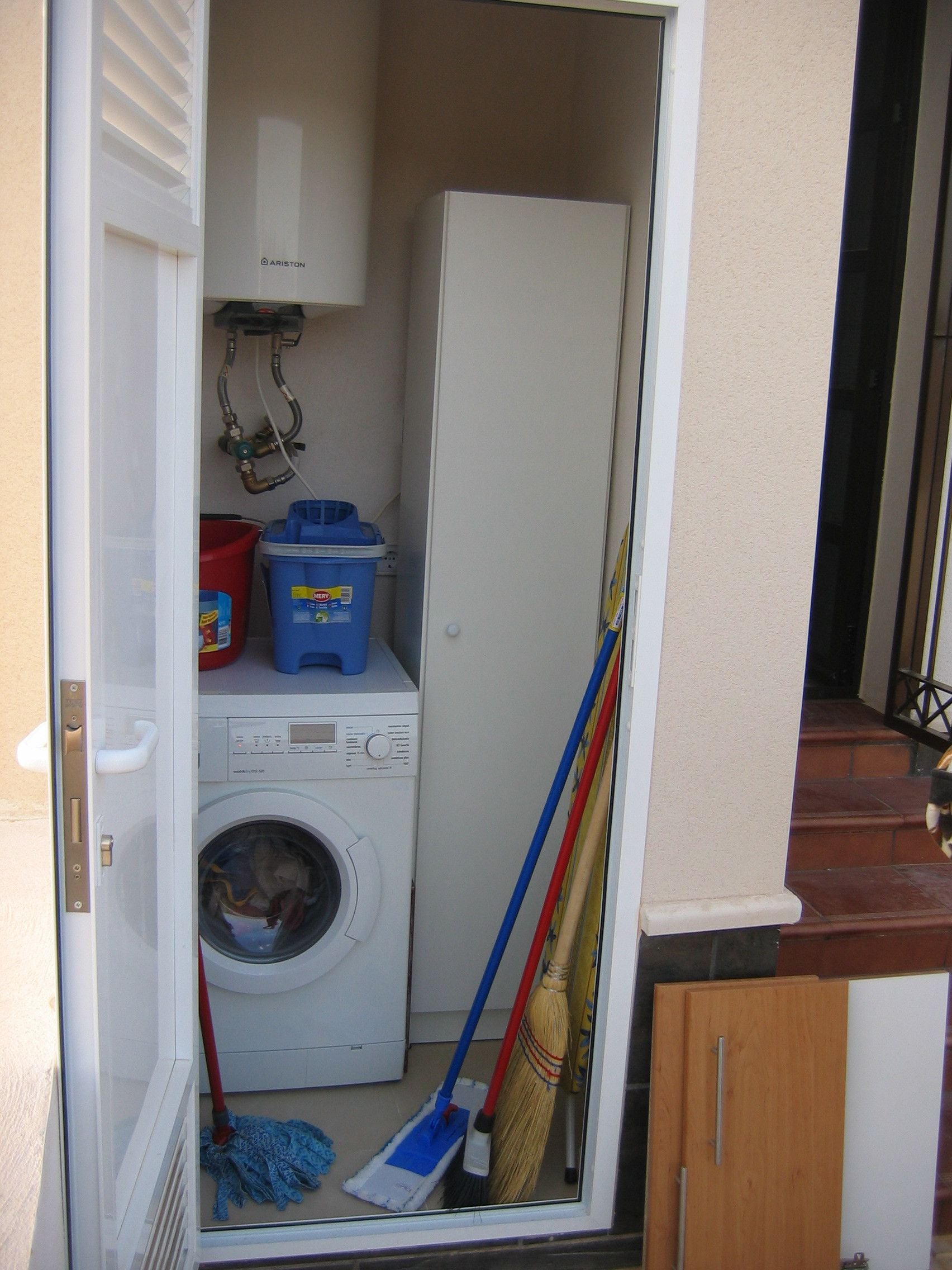 A laundry room with a washing machine, a mop, brooms, and cleaning supplies.