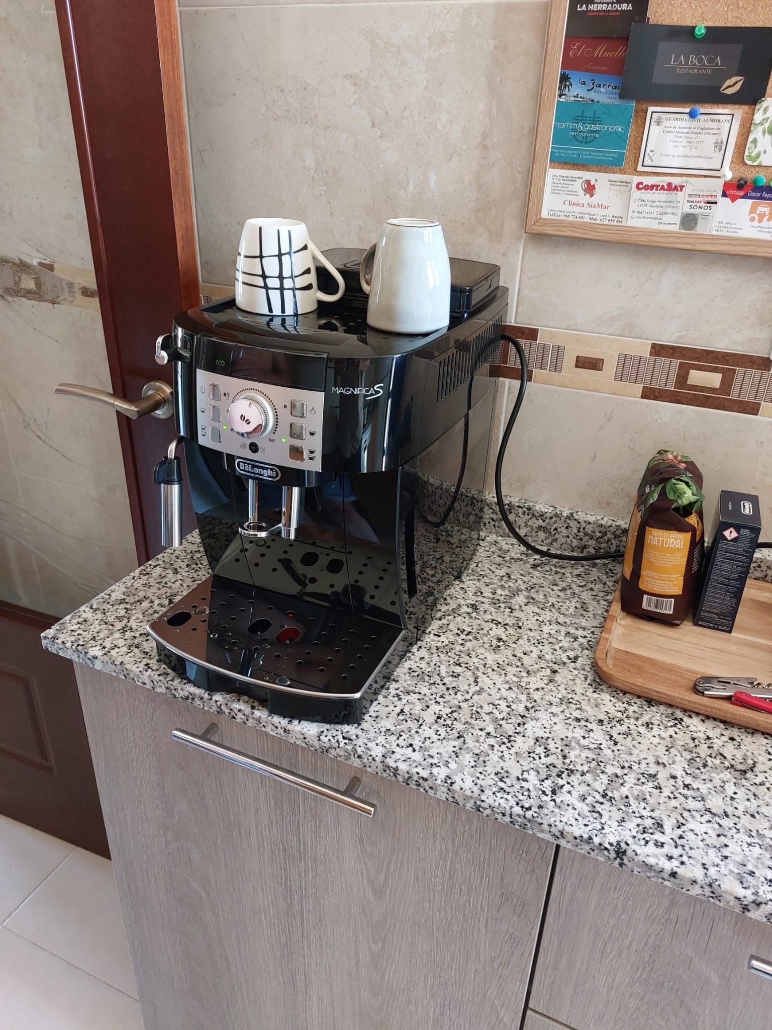 A coffee machine on a granite countertop with a wooden cabinet below.