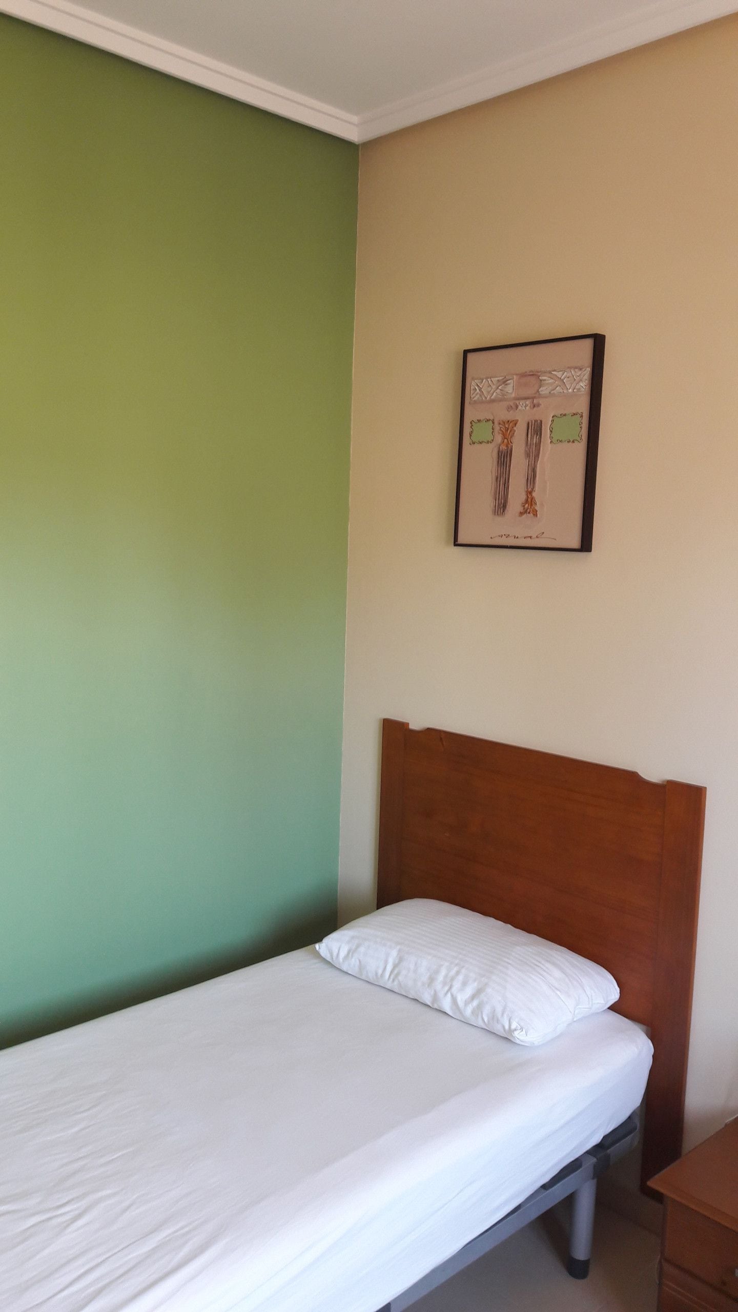 Una cama individual con cabecera de madera en una habitación con paredes verdes y color crema.