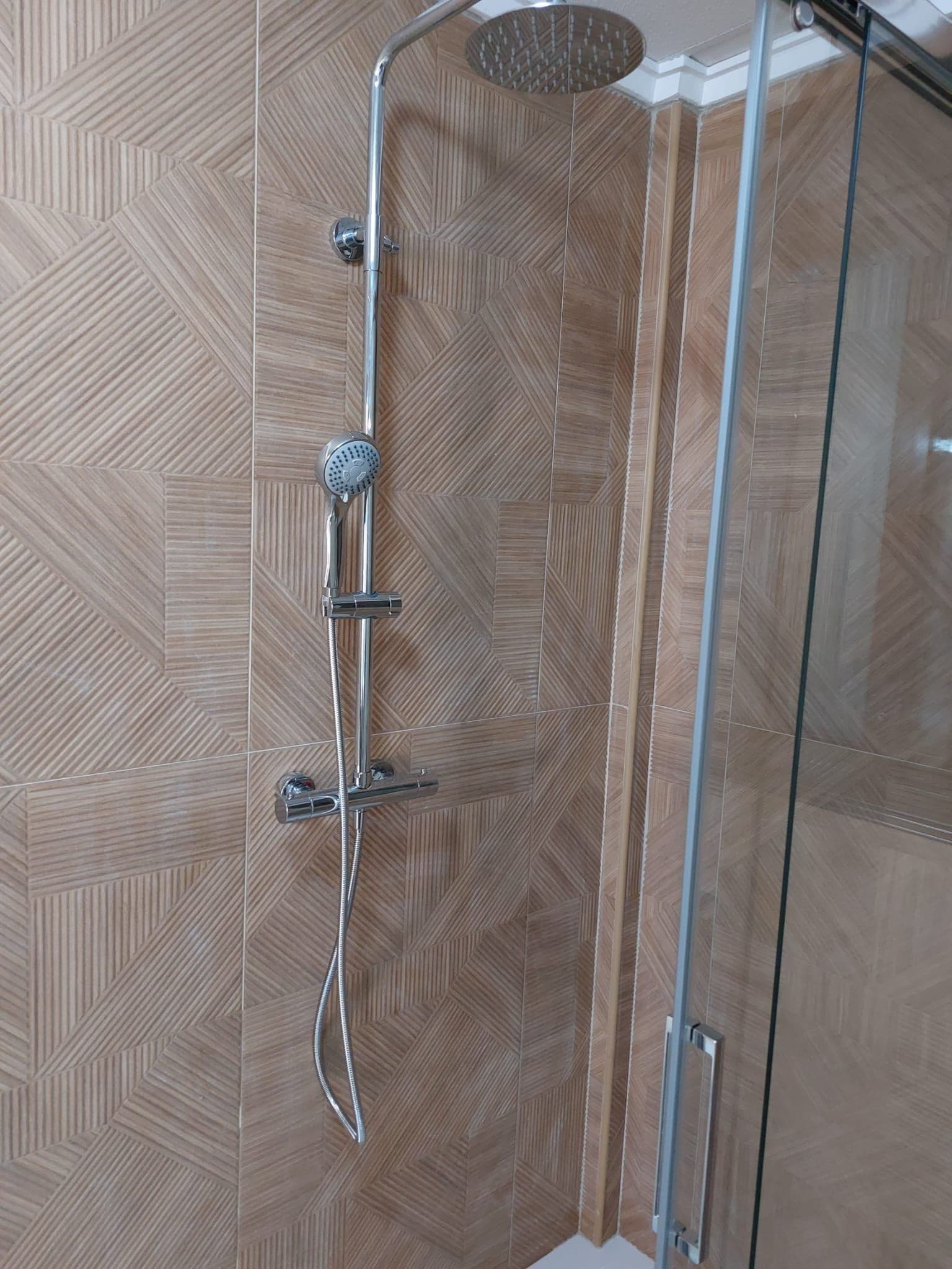 Una ducha moderna con cabezal de ducha de lluvia y otro manual, instalados en una pared con diseño de mosaico hexagonal.