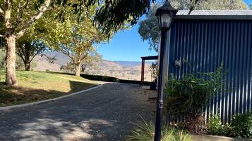 A paved driveway leading to a building with a corrugated metal exterior, surrounded by trees and a clear view of distant hills.