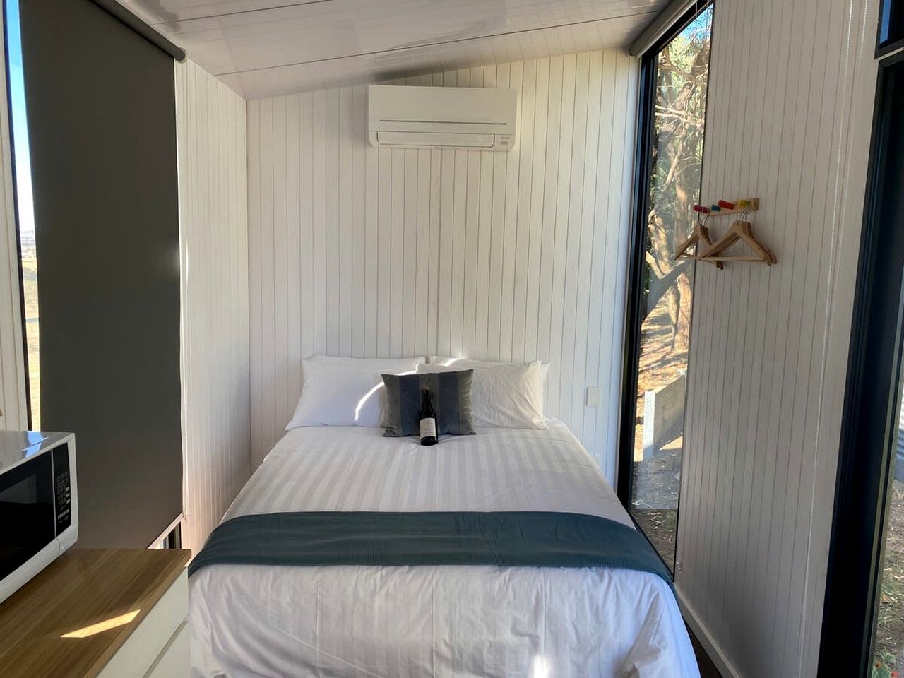 Un dormitorio con cama, almohadas, una mesita de noche, microondas y ventana.
