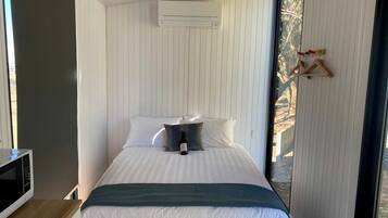 Un dormitorio con cama, almohadas, una mesita de noche, microondas y ventana.