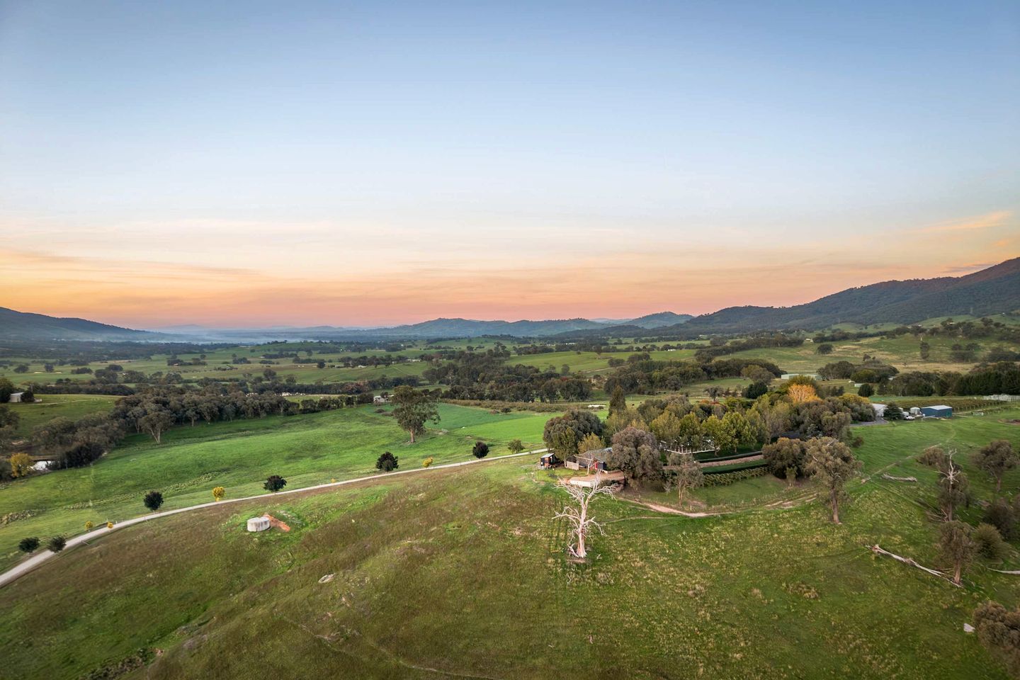 Un paisaje rural con colinas onduladas, un camino sinuoso y edificios dispersos.