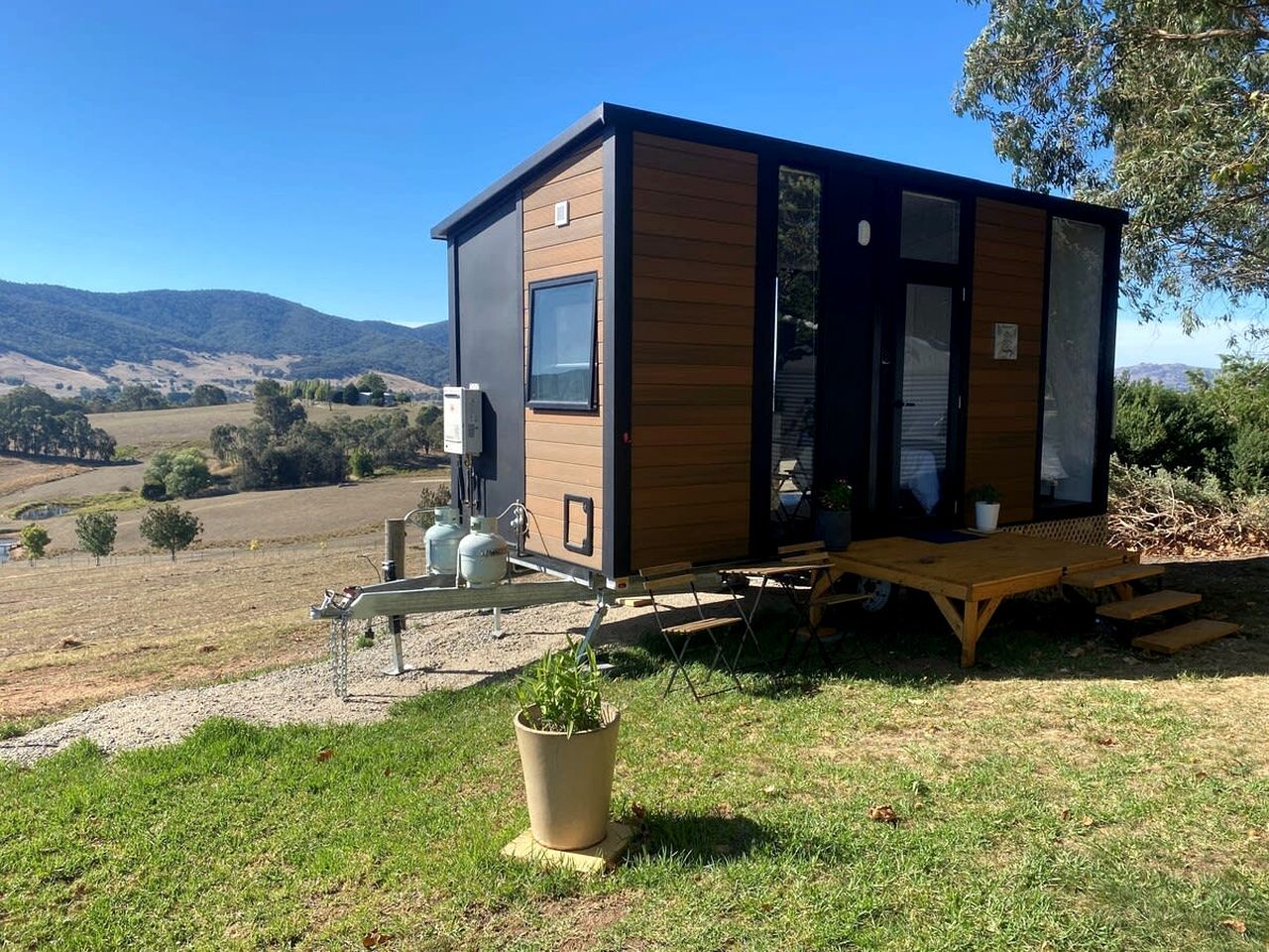 Una casa móvil moderna con techo plano, ventanas amplias y una zona de patio con mesa y sillas.