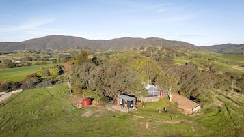 Propiedad rural con una pequeña casa, un granero rojo y una zona cercada.