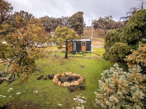 A small cabin with a fire pit in a grassy area surrounded by trees.