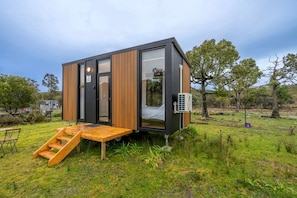 A modern, compact cabin with a wooden exterior, large windows, and a small outdoor seating area.