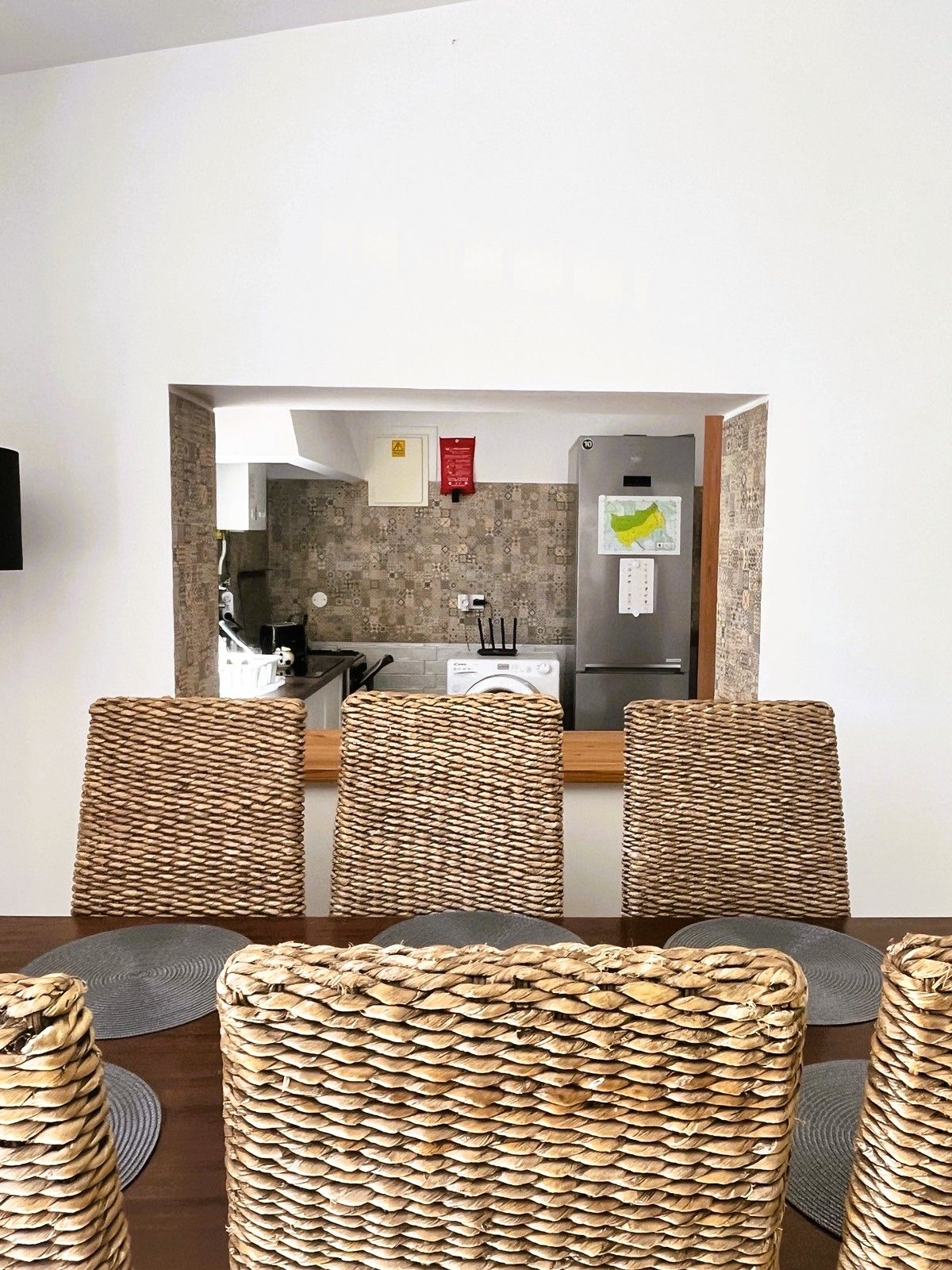 Un comedor con mesa y sillas, una cocina visible a través de un arco, y un detector de incendios instalado en la pared.