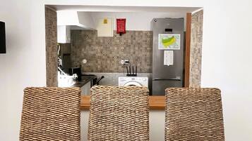 Un comedor con mesa y sillas, una cocina visible a través de un arco, y un detector de incendios instalado en la pared.