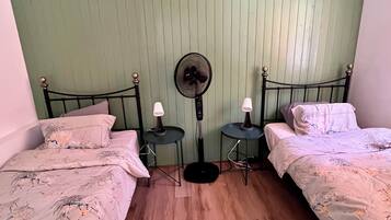 Ein Zimmer mit zwei Betten, einem Standventilator und zwei Nachttischen mit Lampen.