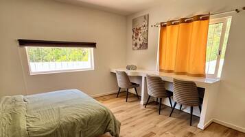 A room with a bed, a desk with chairs, a window with curtains, and a ceiling light.
