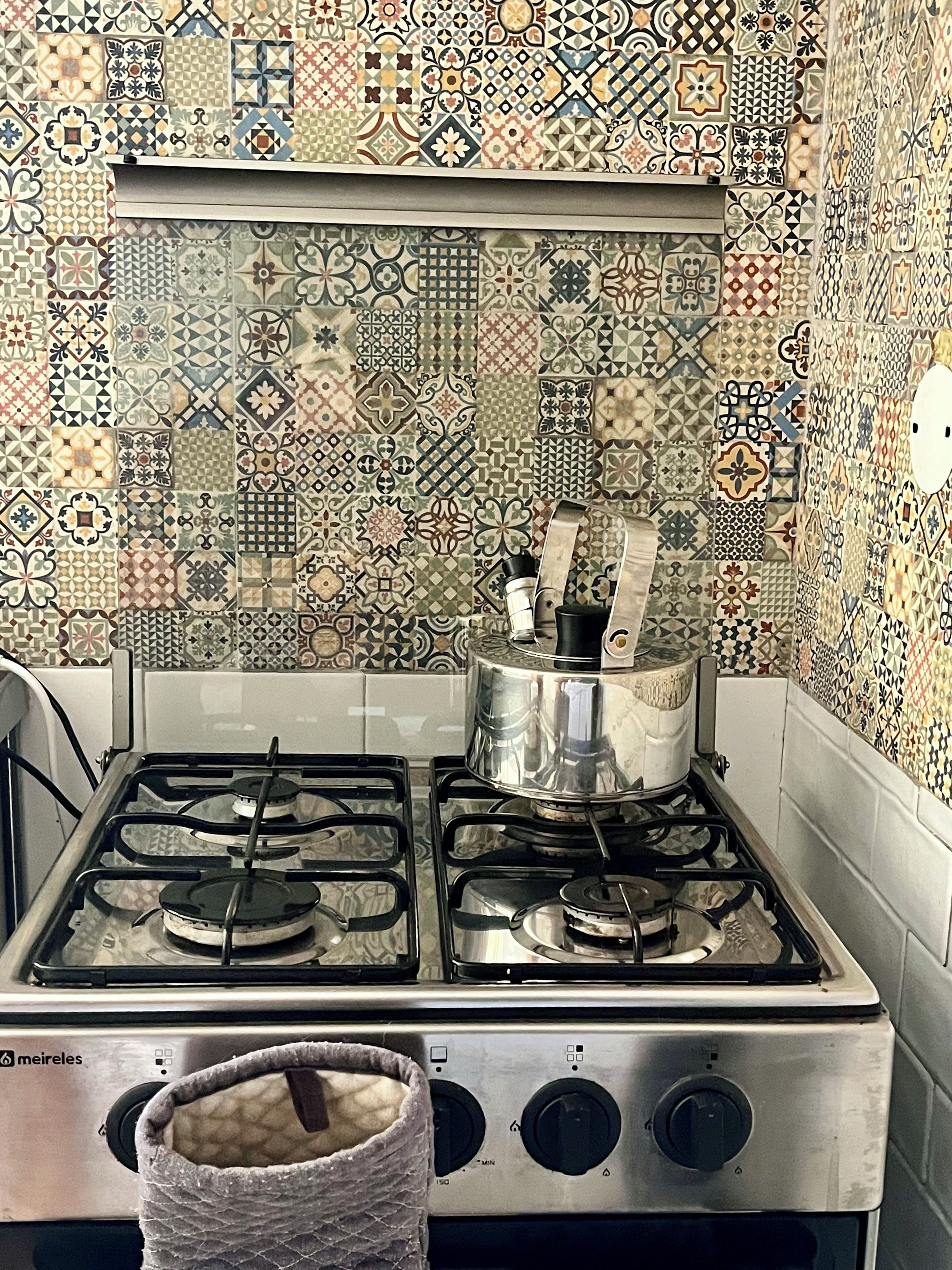 Een keuken met een gasfornuis, een pan op de branders en een betegelde spatwand.