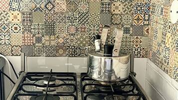 Een keuken met een gasfornuis, een pan op de branders en een betegelde spatwand.