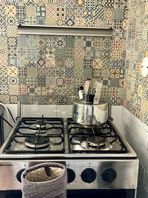 A kitchen with a gas stove, a pot on the burners, and a tiled backsplash.