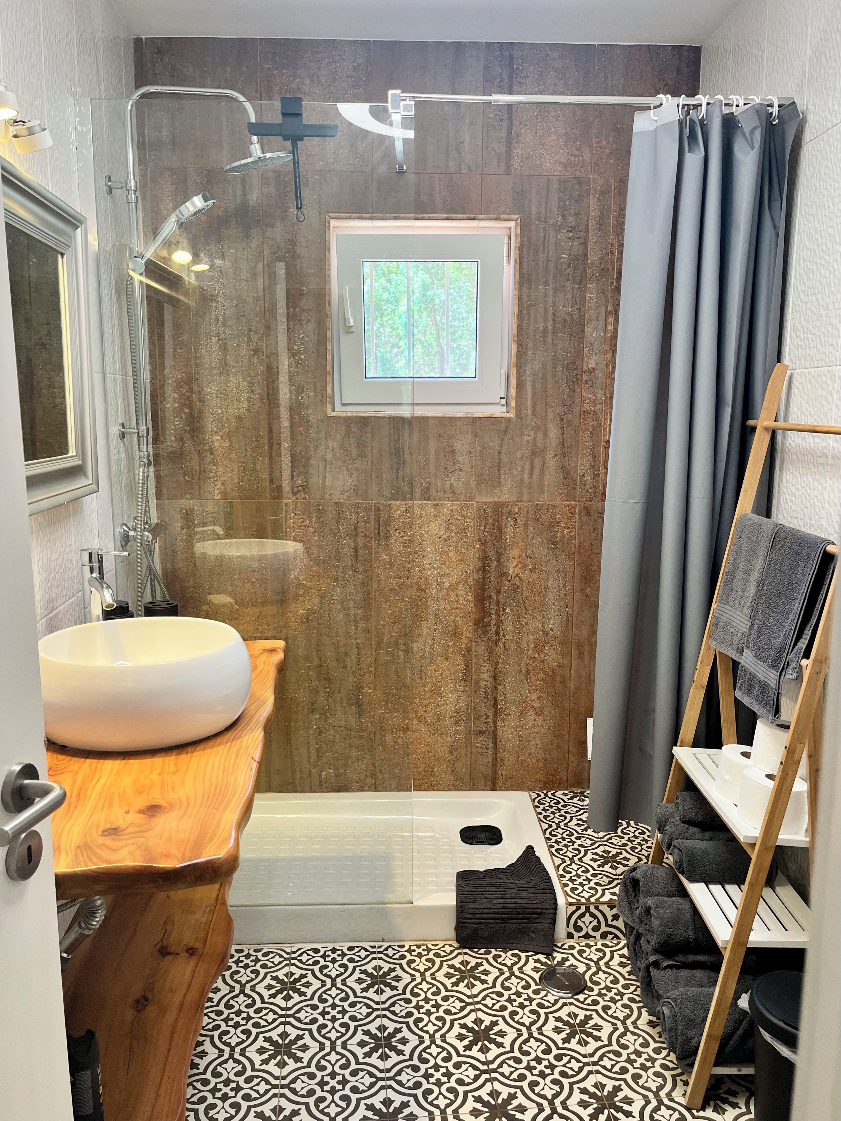 Un baño con tocador de madera, un lavabo redondo, ducha con puerta de vidrio y ventana.