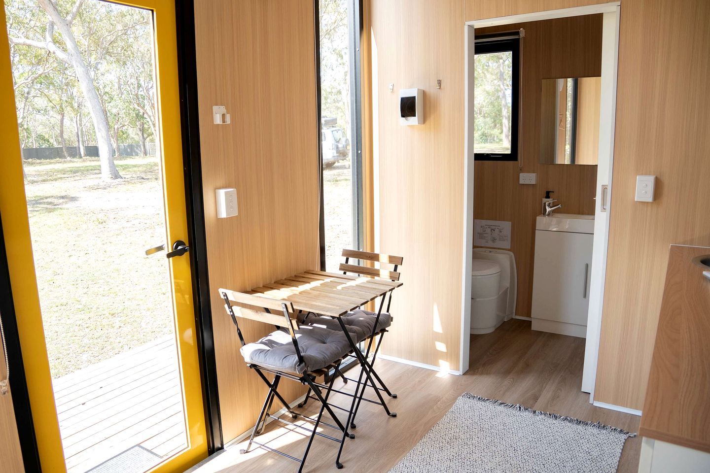A compact room with a wooden table and chairs, a small kitchenette, and a view of the outdoors.
