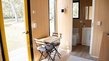 A compact room with a wooden table and chairs, a small kitchenette, and a view of the outdoors.