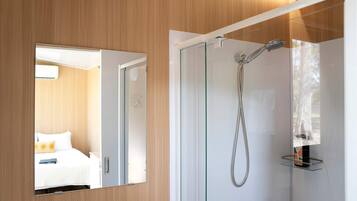 Ein modernes Badezimmer mit einer Duschkabine aus Glas, einem sichtbaren Handtuchhalter und ein Bett mit weißem Kopfteil im angrenzenden Zimmer.