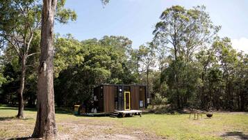 A small, single-story cabin with a wooden exterior and a yellow door, surrounded by trees in a natural setting.